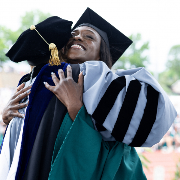 Joyful Washington University in St. Louis student shares a heartwarming hug with the degree awarder during the recognition ceremony, celebrating their achievement.