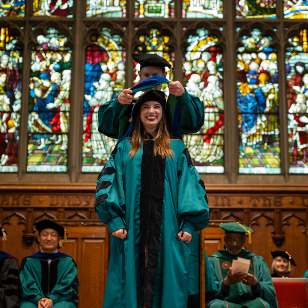 Eager Washington University in St. Louis graduate student wearing a smile while being hooded during the ceremony in Graham Memorial Chapel, symbolizing their academic accomplishment.