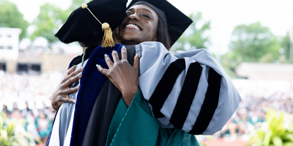 Joyful Washington University in St. Louis student shares a heartwarming hug with the degree awarder during the recognition ceremony, celebrating their achievement.