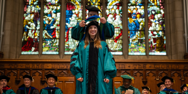 Eager Washington University in St. Louis graduate student wearing a smile while being hooded during the ceremony in Graham Memorial Chapel, symbolizing their academic accomplishment.