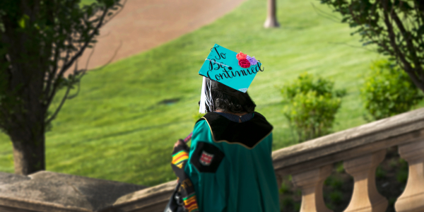 Washington University in St. Louis graduating student in academic attire, including a cap adorned with flowers and the words 'to be continued,' descends outdoor campus stairs, symbolizing their transition to future opportunities and achievements.